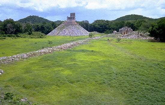 i5-1 A photograph of a restored section of a Maya Sacbe (white road), showing the elevated, straight stone path disappearing into the jungle.