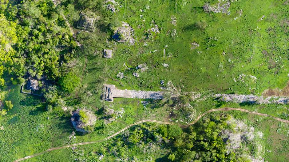 i5 A photograph of a restored section of a Maya Sacbe (white road), showing the elevated, straight stone path disappearing into the jungle.